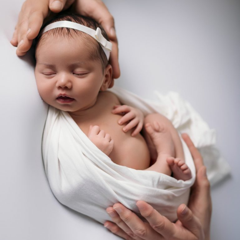 Bebé recién nacido en pose fetal sobre manta blanca en estudio de fotografía en San Fernando