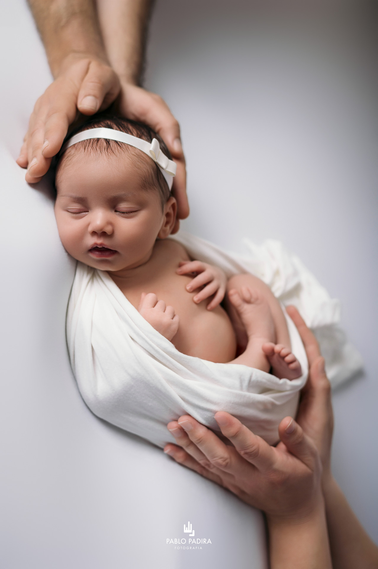 Bebé recién nacido en pose fetal sobre manta blanca en estudio de fotografía en San Fernando